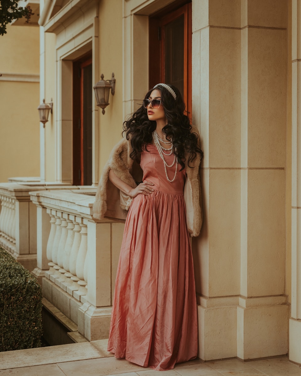 a woman in a long dress leaning against a wall